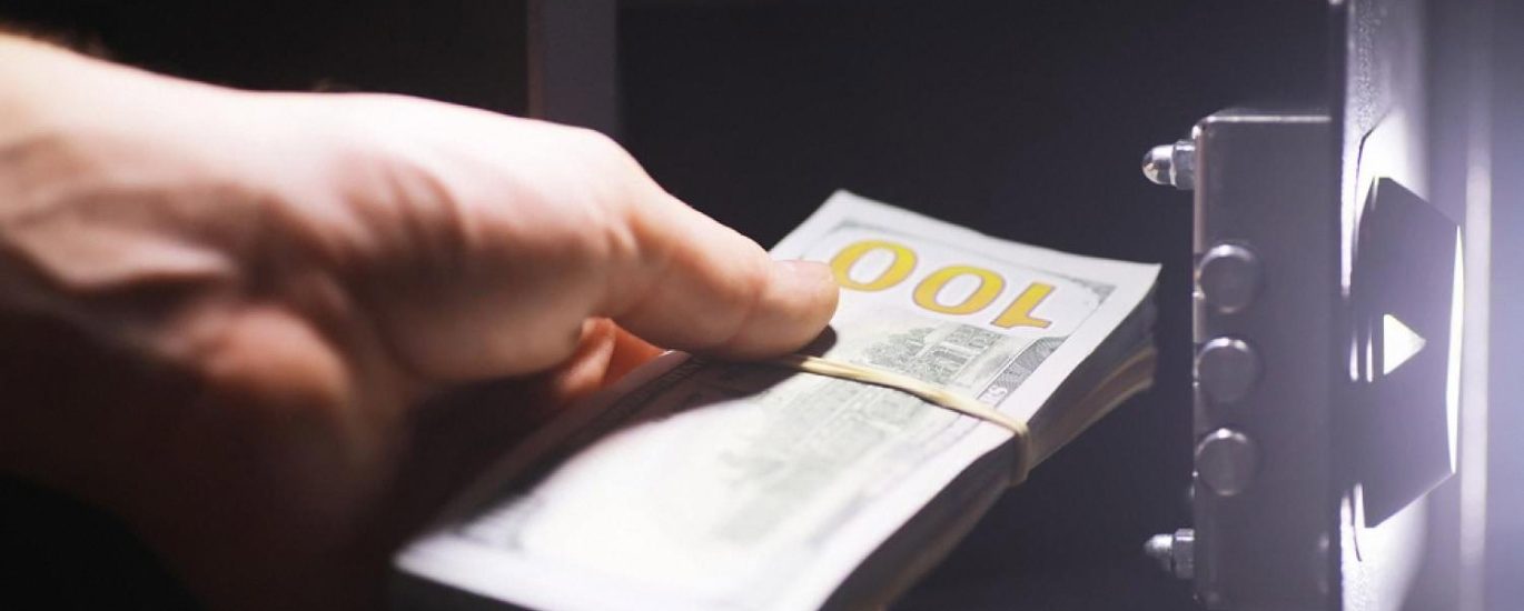 Hand placing a bundle of cash into an open home safe at night
